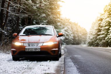 03.12.2020 Minsk, Belarus: Portakal rengi Honda Civic 2008, karlı bir çam ormanında güneş ışınları ile birlikte asfalt yolda farlar yanıyor
