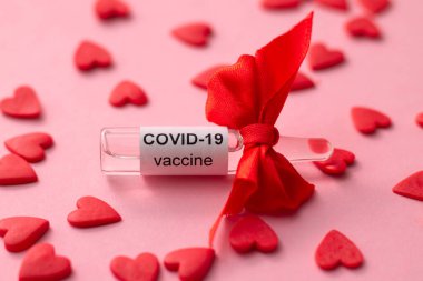 Sevgililer Günü hediyesi olarak COVID-19 aşısı ve pembe arka planda kırmızı kalpler.