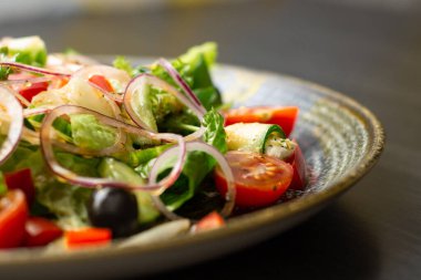 Sebzeli salata, yeşillikler ve ahşap masadaki koyu kil tabakta zeytin.