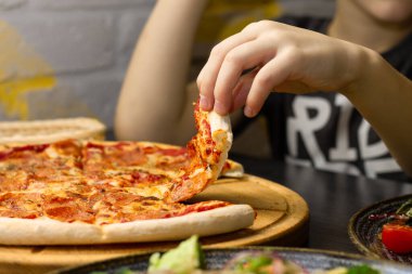 Yuvarlak ahşap tepsiden bir dilim pepperonili pizza alıyorum.