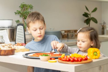 Gri elbiseli tatlı küçük kız 2-4 ve mutfakta pizza pişiren tişörtlü çocuk 7-10. Erkek ve kız kardeş yemeği.