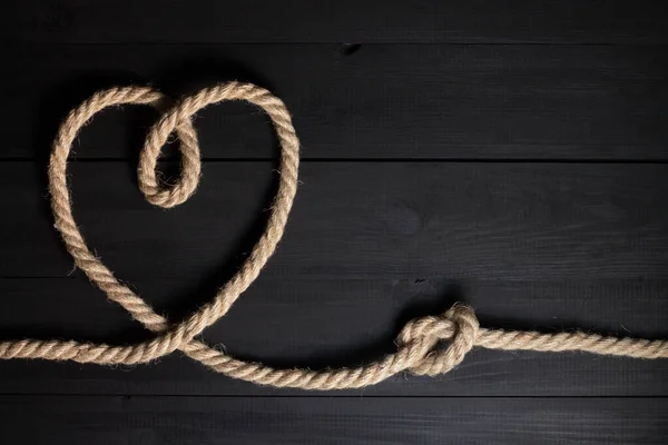 Heart and rope knot on a black wooden background, flat lay