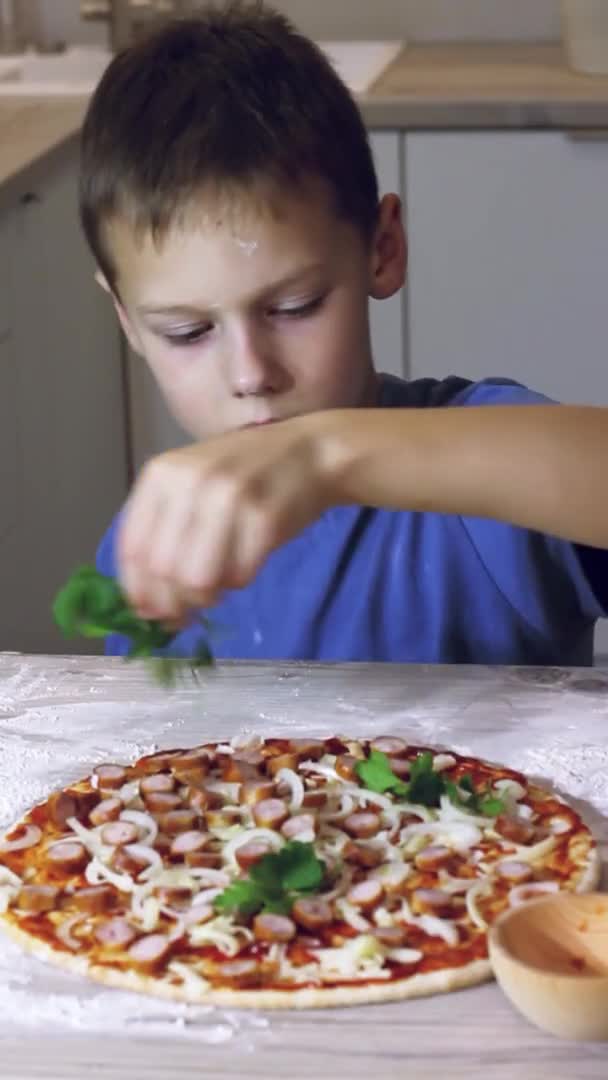 Menino 7-10 em t-shirt cozinhar pizza na cozinha. O miúdo sorri e aponta o dedo à pizza. Vertical — Vídeo de Stock