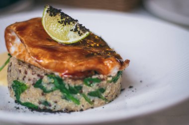 Kısmen bulanık tabakta kinoa tabağı, sos, turna balığı ve limon dilimi.