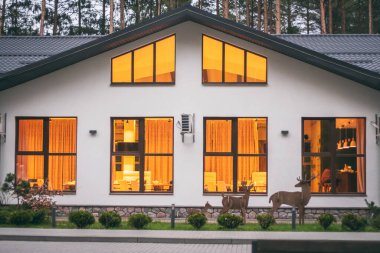 Çam ormanlarında çatısı olan, geniş pencereli, yanan ışıkları olan beyaz restoran binası.