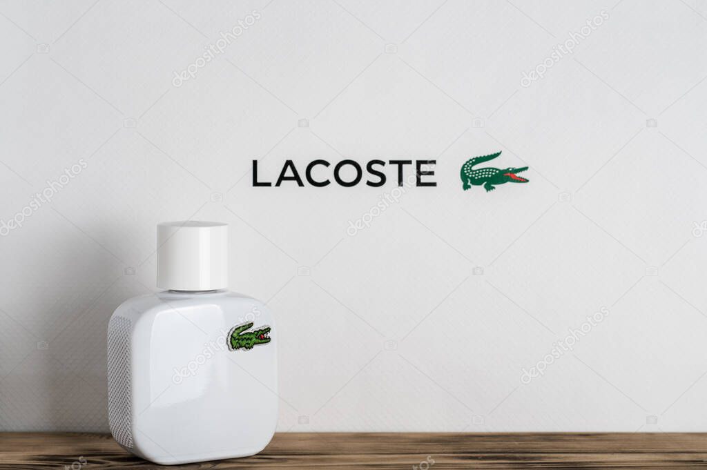 Minsk, Belarus 07.05.2021: Minsk, Belarus 07.05.2021: Minsk, Belarus 07.05.2021: Minsk, Belarus 07.05.2021: White open perfume bottle with Lacoste logo on wet surface with drops on white and monstera leaf background
