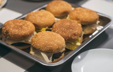 Masadaki metal tepside susamlı ev yapımı burgerler.