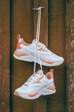 Beyaz kadınların spor ayakkabıları, üzerinde mercan parçaları olan kahverengi tahta duvarlarda asılı duran tahta çiviler. Dikey