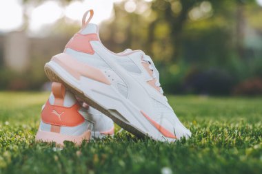 Minsk, Belarus, 23.05.2021: Mercan yerleştirilmiş beyaz kadın PUMA ayakkabıları güneş ışığı ışınlarında çimlerin üzerinde duruyor