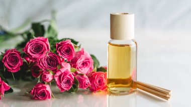 Açık sarı yağ şişesi ya da ahşap sopalı parfüm ve beyaz yüzeyde pembe güller. SPA salonu ve prosedür konsepti. Pankart. Boşluğu kopyala