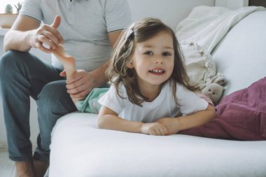 Babası küçük kızıyla kanepede 2-4 oynuyor. Babam çocukların ayaklarını gıdıklıyor. Ailem eğleniyor.