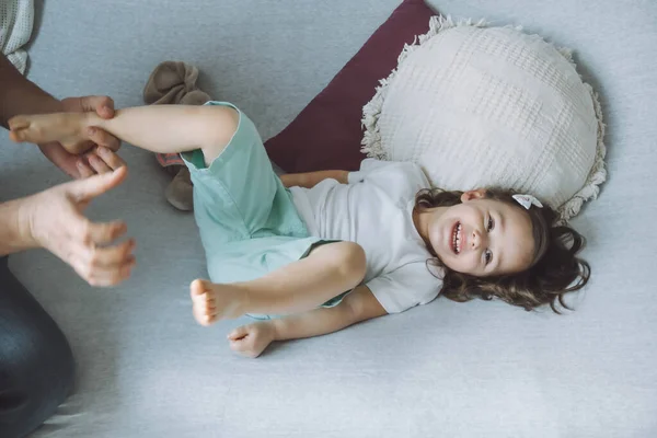 Father plays with little daughter 2-4 on couch. Dad tickles kids feet. Family, having fun