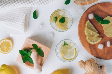 İki bardak limonata ve yemek malzemeleri. Zencefil, limon, nane, beyaz yüzeyde buz. Tahta tepsi, havan topu ve tokmak. Düz yatıyordu