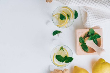 İki bardak limonata ve yemek malzemeleri. Zencefil, limon, nane, beyaz yüzeyde buz. Tahta havan ve tokmak. Düz yatıyordu. Üst Manzara. Boşluğu kopyala
