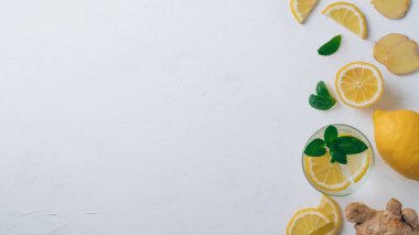 Bir bardak limonata ve yemek malzemeleri. Zencefil, limon, beyaz yüzeyde nane. Düz yatıyordu. Üst Manzara. Uzayı kopyala Pankart