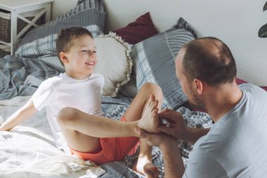 Baba oğluyla yatakta 7-10 oynuyor. Babam çocukların ayaklarını gıdıklıyor. Ailem eğleniyor.