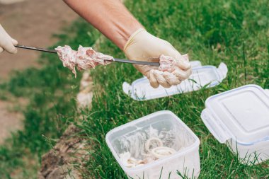 Beyaz eldivenli erkek eller mangal yapmak için salamura edilmiş çiğ eti şişe diziyor.