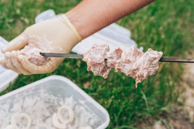 Beyaz eldivenli erkek eller mangal yapmak için salamura edilmiş çiğ eti şişe diziyor.
