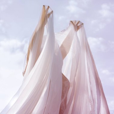 Peçeli ya da ince kumaşlı bir kadın elleri havada gökyüzüne karşı durur.