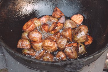 Bahçe kazanında pişirilmiş patates ve içinde yakacak odun ve bol miktarda kaynayan ayçiçeği yağı var.