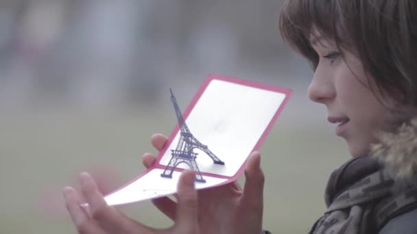Piękna młoda kobieta, patrząc na wieży Eiffel Paris pocztówka. — Wideo stockowe