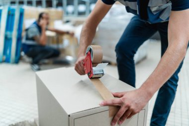 Depo işçisinin paket paketlediği yakın plan fotoğraf.