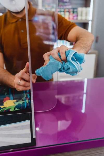 Retail store manager cleaning protective glass during virus pandemic