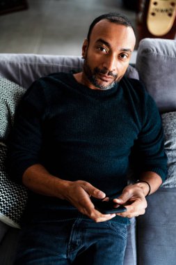 40 yaşında bir adam evdeki kanepede dinleniyor ve telefonda konuşuyor.