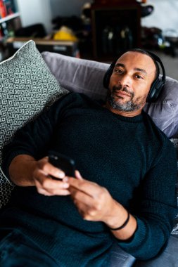 Karışık ırk adamı evde dinleniyor ve müzik dinliyor.