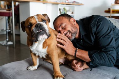 40 yaşında bir adam evdeki kanepede köpeğiyle oynuyor ve telefonda konuşuyor.