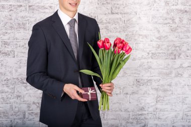 Çiçek ve hediye kutusu üzerinde beyaz geri tutarak gülümseyen iş adamı