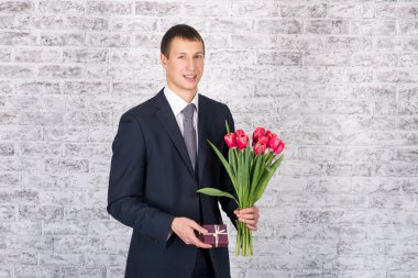Çiçek ve hediye kutusu üzerinde beyaz geri tutarak gülümseyen iş adamı