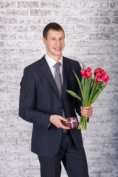 Smiling businessman holding flowers and gift box over white back — Stock Photo, Image