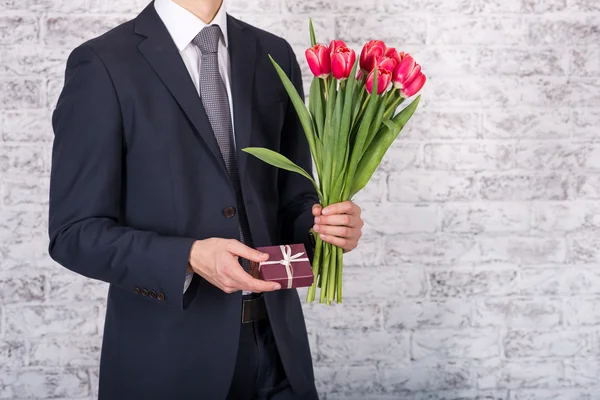 Çiçek ve hediye kutusu üzerinde beyaz geri tutarak gülümseyen iş adamı