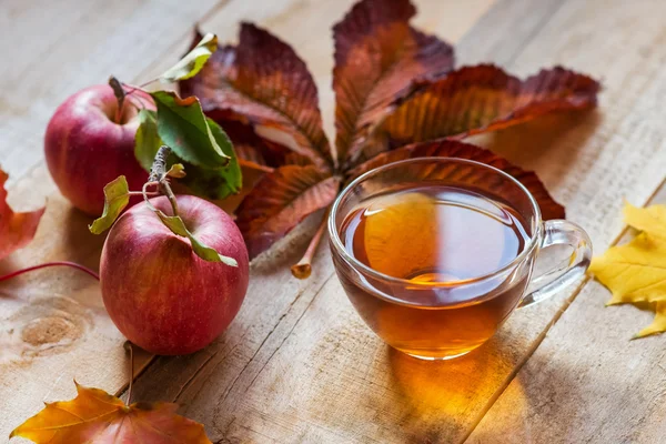 Glas heißen Tee auf einem Holztisch mit Herbstblättern und ap — Stockfoto