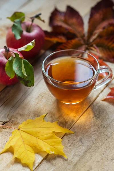 Taza de té caliente de vidrio en una mesa de madera con hojas de otoño y ap — Foto de Stock