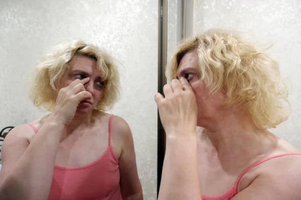 깨어 있는 한 여자가 거울 앞에 서서 눈의 모서리를 문지르고 있다. — 스톡 사진