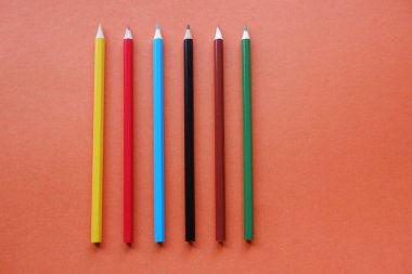 Turuncu arka planda renkli kalemler. 1 Eylül bilgi günüdür.