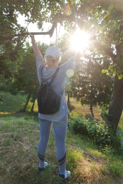 Beyaz şapkalı bir turist kız güneşle buluşmak için ellerini kaldırıyor..