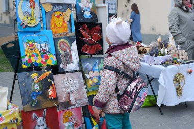 Küçük bir kız sokakta sergilenen düzinelerce resme değer biçerek bakıyor..