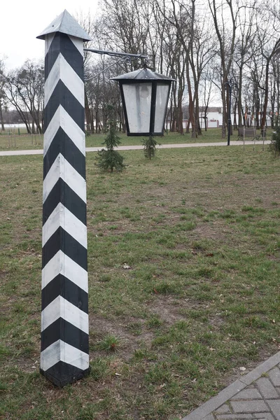 Sculpture of an old border pillar in black and white stripes and a lantern hanging from it. — Stock Photo, Image