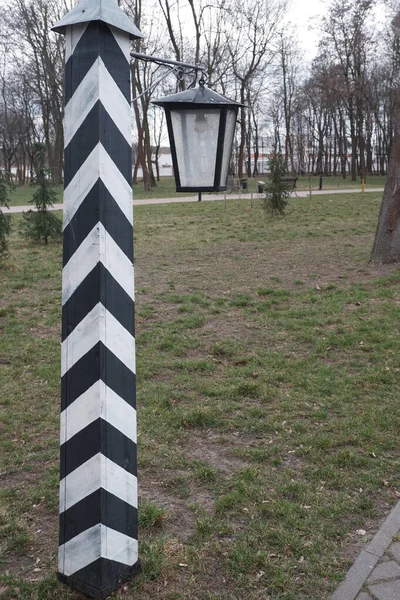 Sculpture of an old border pillar in black and white stripes and a lantern hanging from it. — Stock Photo, Image