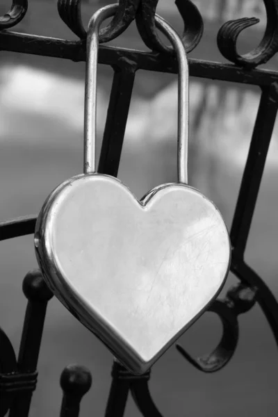 Metal silver door lock in the shape of a heart on the fence as a symbol of eternal love.