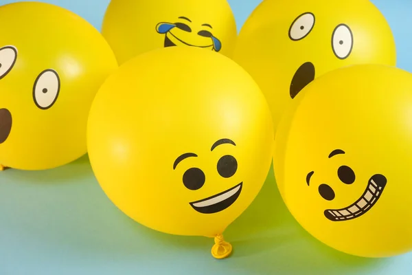 Mavi arka planda sarı emoji balonları.