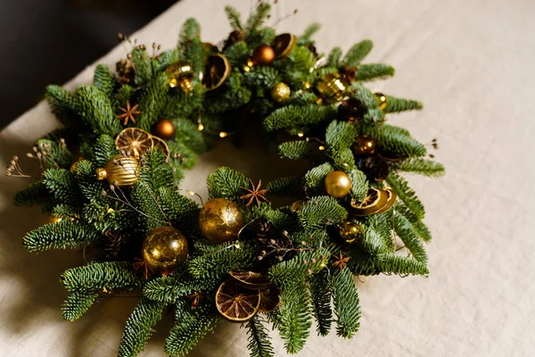 Beautiful Christmas spruce wreath. Handmade new year eco decoration closeup. Decor elements are yellow and golden glass balls, cones, star anise and dried mugs of lime and orange.