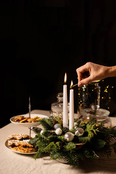 Kadın el feneri iki beyaz mum. Keten masa örtüsünde geleneksel kurabiyelerle süslenmiş bir masa. Metin için kopyalama alanı olan siyah arkaplan. Xmas hazırlığı ve yeni yıl kutlaması konsepti