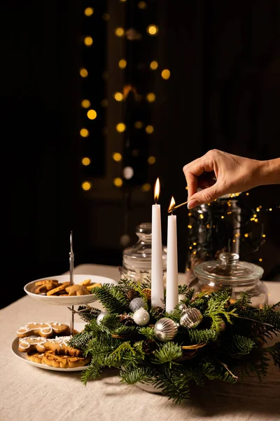 Xmas dekorasyonu ve keten masa örtüsü üzerinde geleneksel kurabiyeler. Kadın el feneri iki beyaz mum. Altın bokeh ışıkları siyah arka planda parlıyor. Tatil hazırlığı ve yeni yıl kutlaması konsepti