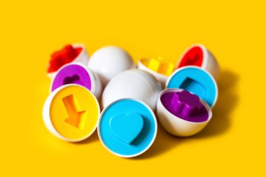 Sarı arka planda çok renkli plastik yumurtalar. Bebeklerin renkleri ve şekilleri tanıması ve eşleştirmesi için eğitici bir oyuncak. Bulmaca montessori oyun konsepti. Yakın plan, metin için boşluk kopyala