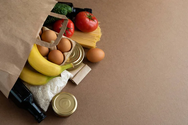 Χάρτινη τσάντα με προμήθειες τροφίμων σε ουδέτερο μπεζ φόντο. Ζυμαρικά, ρύζι, λάδι, ξύδι, αυγά, μπανάνες, ντομάτες, κονσέρβες, αγγούρια, μπαχαρικά. Παράδοση για καραντίνα, ιδέα δωρεάς. Αντιγραφή κενού κειμένου — Φωτογραφία Αρχείου