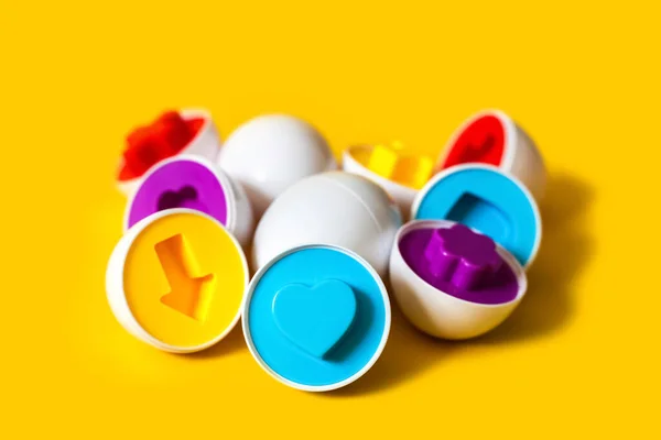 Sarı arka planda çok renkli plastik yumurtalar. Bebeklerin renkleri ve şekilleri tanıması ve eşleştirmesi için eğitici bir oyuncak. Bulmaca montessori oyun konsepti. Yakın plan, metin için boşluk kopyala